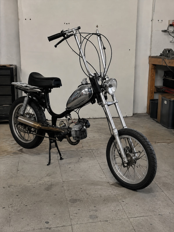 Inspirés du film « Easy Rider », les Alpa Chopper ont une longue fourche et un guidon relevé. Vue de face d’un Alpa Chopper noir dans un garage