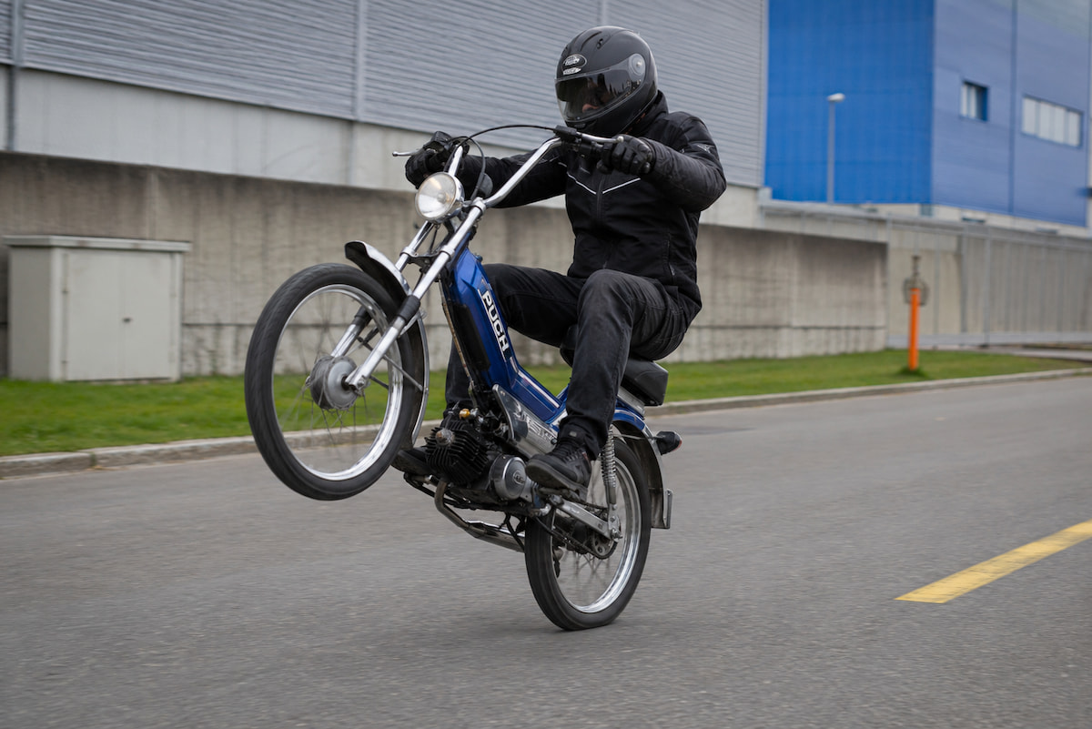 Mann macht Wheelie auf blauem Puch Töffli