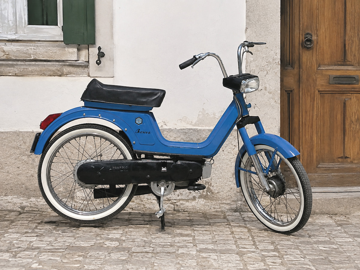 Einer der Unterschiede zwischen Boxer 1 und Boxer 2 sind die grösseren Reifen des Boxer 1 - serienmässig liefen diese Töfflis auf 18" Pneus. Blaues Piaggio Boxer 1 Töffli vor Hauswand