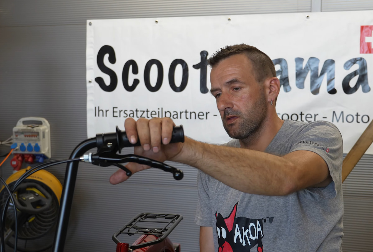 Homme vérifiant le câble d'accélérateur de son vélomoteur au braquage